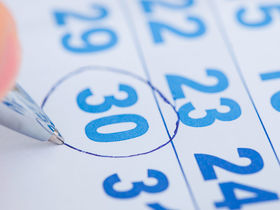 Eine Person kreist die Zahl 30 auf einem Kalenderblatt mit einem Kugelschreiber ein.